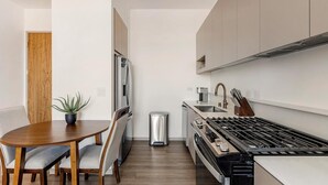 Een compacte keuken met een eethoek, roestvrijstalen apparatuur en een kleine prullenbak.