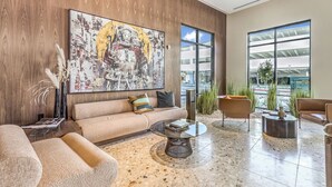Een moderne lobby met een groot abstract schilderij, een bank, een bijzettafeltje en uitzicht op buiten door grote ramen.