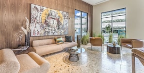 A modern lobby with a large abstract painting, a sofa, a coffee table, and a view of the outside through large windows. - Landing | Chic 1BD, Gym, Pool (Enterprise)