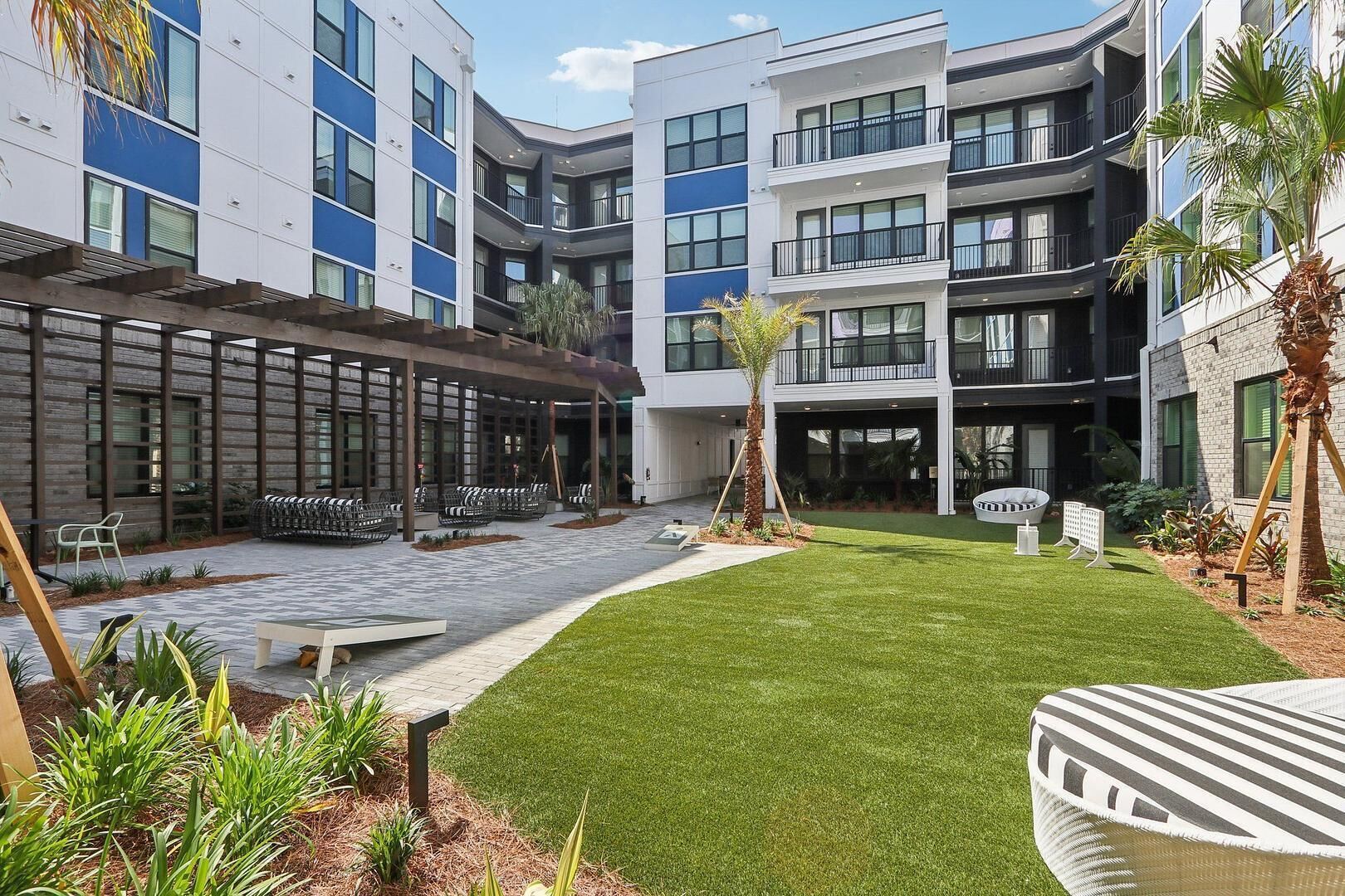 Un patio con césped, mobiliario exterior y edificios modernos con balcones.