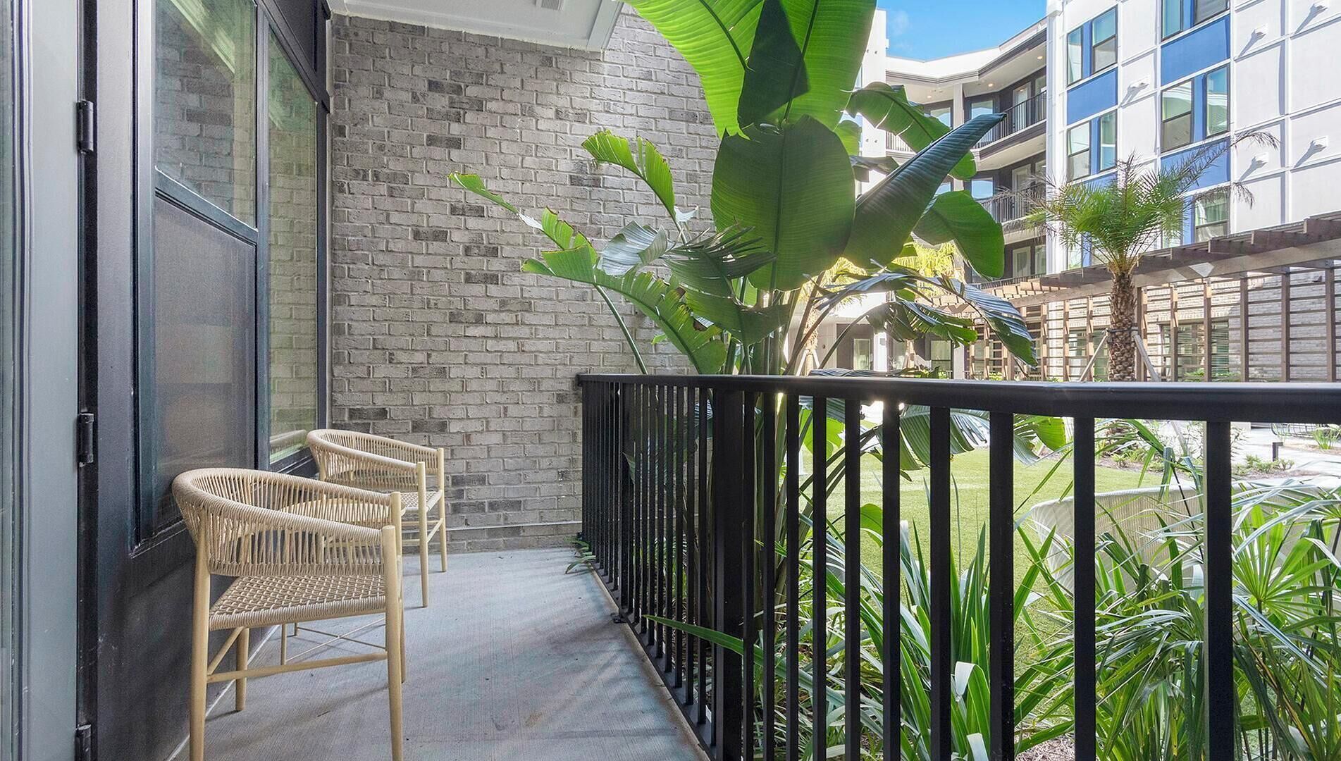 A balcony with wicker chairs, a brick wall, and a view of a building with large windows.