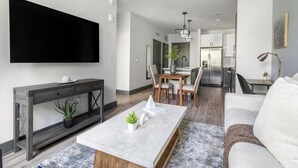 Ein modernes Wohnzimmer mit Flachbildfernseher, Couchtisch mit Dekoration, Sofa und Essbereich mit Stühlen und Tisch.