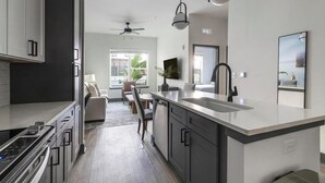 A modern kitchen with a large island, built-in appliances, and a dining area with a sofa and chairs. - Landing | Incredible 1BD, Rooftop Lounge (Jacksonville)