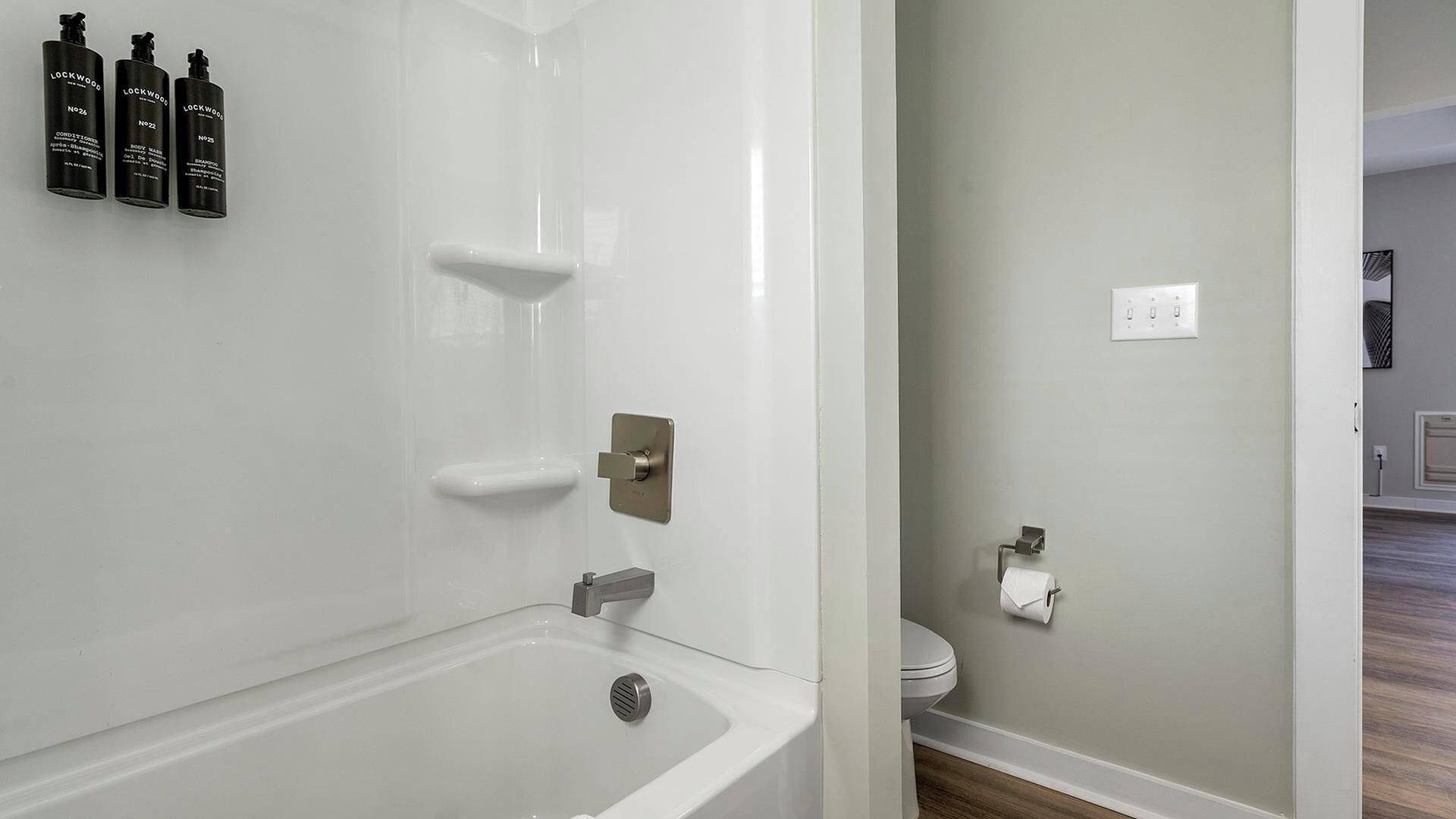 Et moderne badeværelse med badekar, bruser og toilet. Der er tre flasker Lockwood badesæbe på væggen.