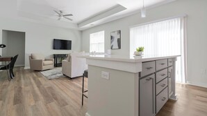 Una cocina moderna con una isla central, zona de comedor con sillas, un sofá y un televisor de pantalla plana.