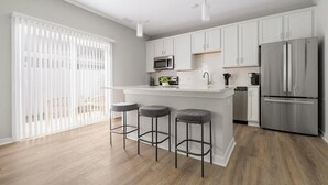 Una cocina moderna con armarios blancos, electrodomésticos de acero inoxidable y una zona con taburetes de bar.
