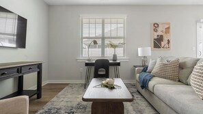 Ein modernes Wohnzimmer mit einer Couch, einem Couchtisch, einem Schreibtisch und einem Fenster mit Jalousien.