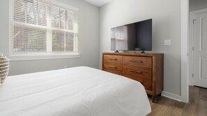 A bedroom with a bed, a dresser, a TV on the dresser, and a window with blinds. - Landing | Spectacular 1BD, Gym, Courtyard (Charlotte)