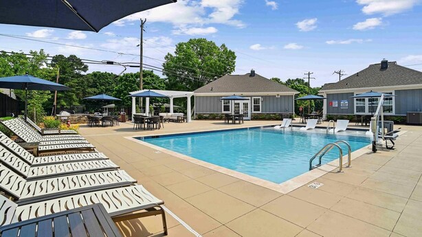 Ein Pool mit Liegestühlen und Sonnenschirmen, umgeben von einer überdachten Terrasse mit Tischen und Stühlen.