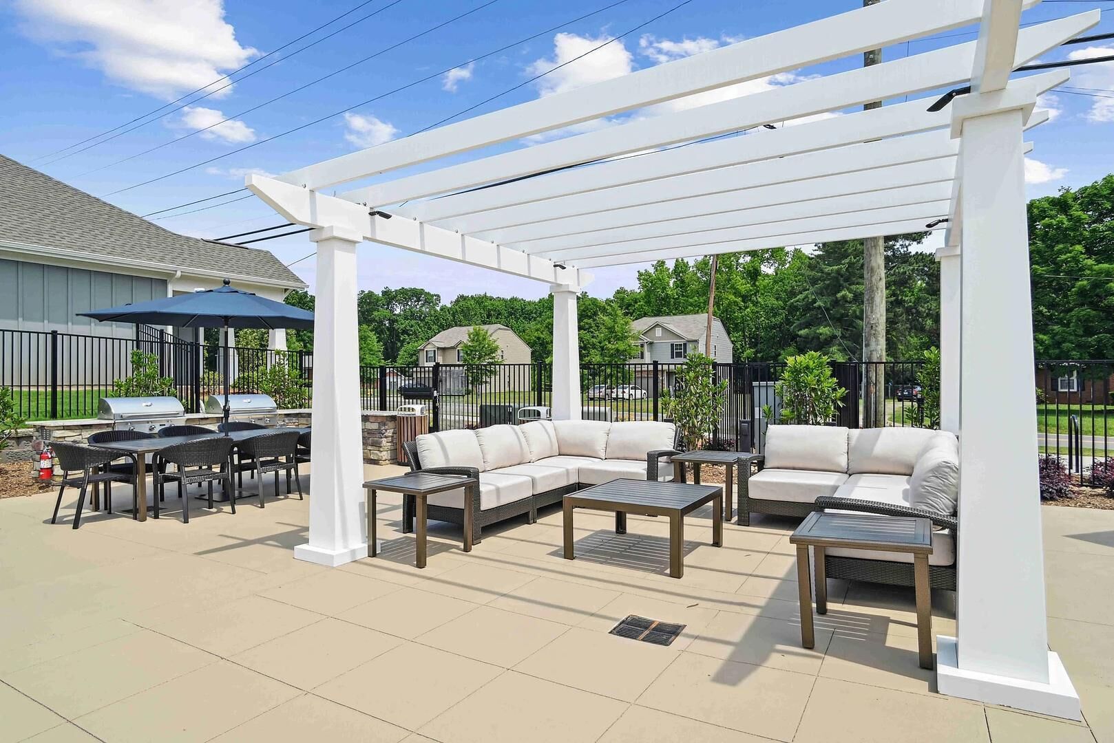An outdoor patio area with a white pergola, a grill, a sofa, and a dining table.
