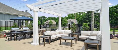 Un espace extérieur aménagé avec une pergola blanche, un barbecue, un canapé et une table à manger.
