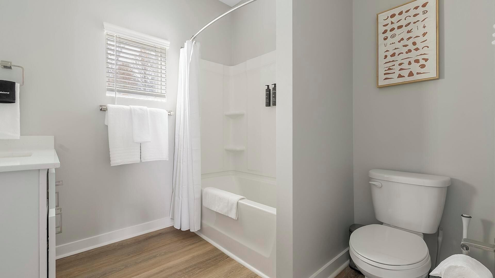 A bathroom with a shower, toilet, and a window with blinds.