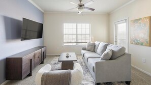 A living room with a flat-screen TV, a sofa, a coffee table, and a ceiling fan.