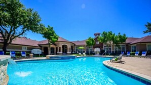 A swimming pool with lounge chairs and a covered area, surrounded by buildings with a consistent architectural style. - Landing | Beautiful 2BD, Clubhouse, Gym (Lewisville)