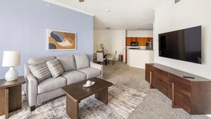 A modern living room with a sofa, coffee table, and TV. There's a kitchen area with wooden cabinets and a microwave. - Landing | Beautiful 2BD, Clubhouse, Gym (Lewisville)