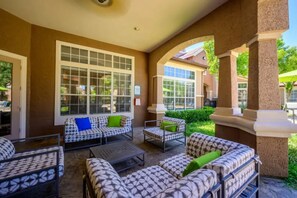 A covered outdoor seating area with patterned furniture and a large window. - Landing | Chic 1BD, Gym, Clubhouse (Lewisville)