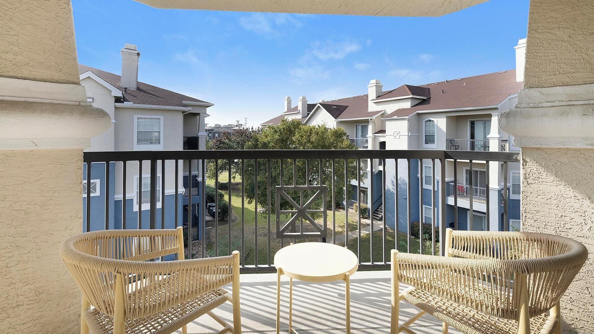 A balcony with wicker furniture and a glass railing overlooking a residential area.