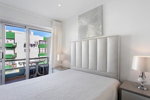 Habitación de hotel con cama, dos mesitas de noche, ventana con vistas a edificios y una obra de arte colgada en la pared.