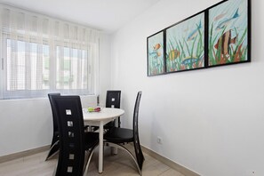 Un comedor con una mesa redonda, sillas negras, una ventana con cortinas translúcidas y tres cuadros enmarcados en la pared.