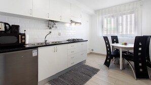 A modern kitchen with white cabinets, a black countertop, and a dining area with a table and chairs. - Natalina T1 Apartment with Balcony and Wi-Fi (Nazaré)