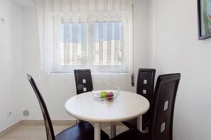 Ein kleiner Essbereich mit einem runden Tisch, vier Stühlen, einem Fenster mit transparenten Vorhängen und einem Wandbild.