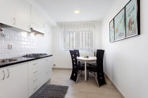 Una cocina con armarios blancos, una estufa a gas y un comedor con mesa y sillas.