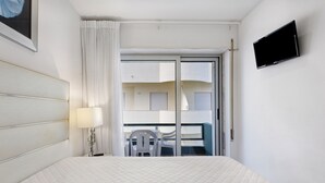 Ein Hotelzimmer mit Bett, Fernseher, Fenster mit Vorhängen und einem Balkon mit Stühlen.