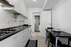 Une cuisine compacte équipée d’une cuisinière, d’un évier et d’un lave-linge, qui donne sur un coin repas avec des chaises et une table.