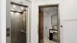 Ein Aufzug mit einem Schild, das die zweite Etage anzeigt, eine Holztür zu einem Badezimmer mit Spiegel und Waschbecken.