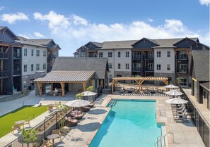 A modern hotel with a central pool, outdoor seating, and a covered patio area.