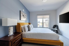 Ein Schlafzimmer mit Bett, Nachttisch, Lampe, Stuhl und einem Fenster mit Jalousien.
