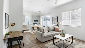 A modern apartment with a dining area, a living room with a sofa and coffee table, a kitchen, and large windows with blinds. - Landing | Amazing 2BD, Gym (Phoenix)