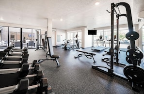 A gym with various exercise equipment, large windows, and a view of the street. - Landing | Stylish 2BD, Gym, Rooftop Lounge (Salt Lake City)
