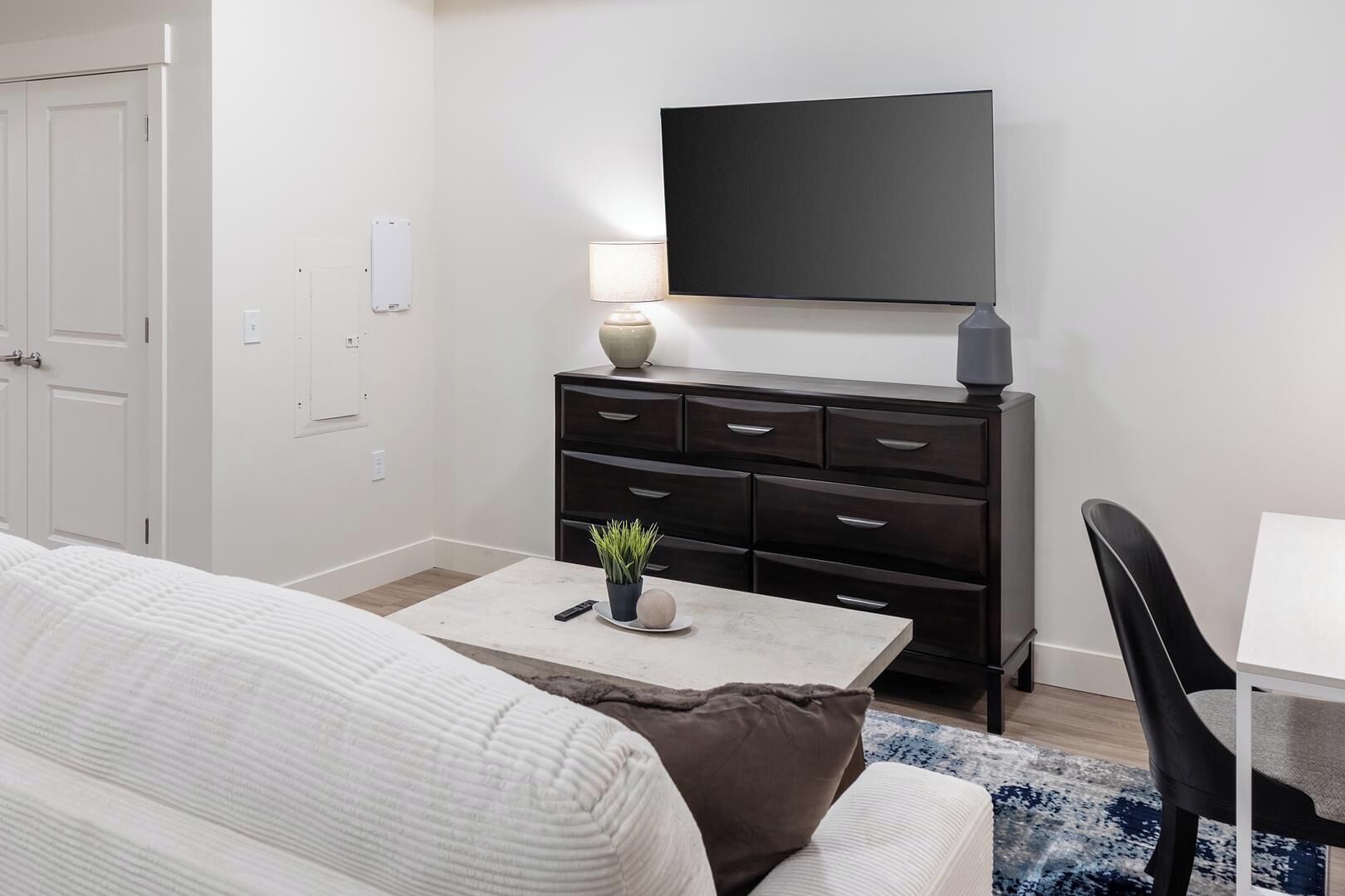 Ett modernt hotellrum med en säng, ett skrivbord med en lampa, en TV och en byrå.