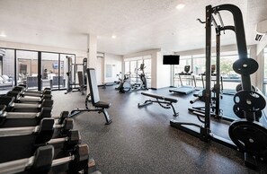 Een sportschool met diverse fitnessapparaten, grote ramen en uitzicht op de straat.