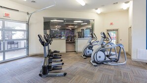 A gym with treadmills and elliptical machines, a glass door leading outside, and an exit sign on the wall. - Landing | Modern 1BD, Clubhouse, Gym (Murfreesboro)