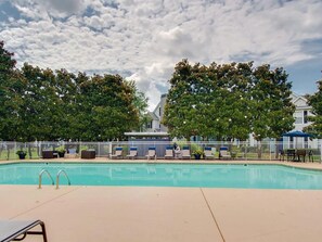 Ein Schwimmbecken mit Liegestühlen und einem Zaun, umgeben von Bäumen und einem Gebäude im Hintergrund.