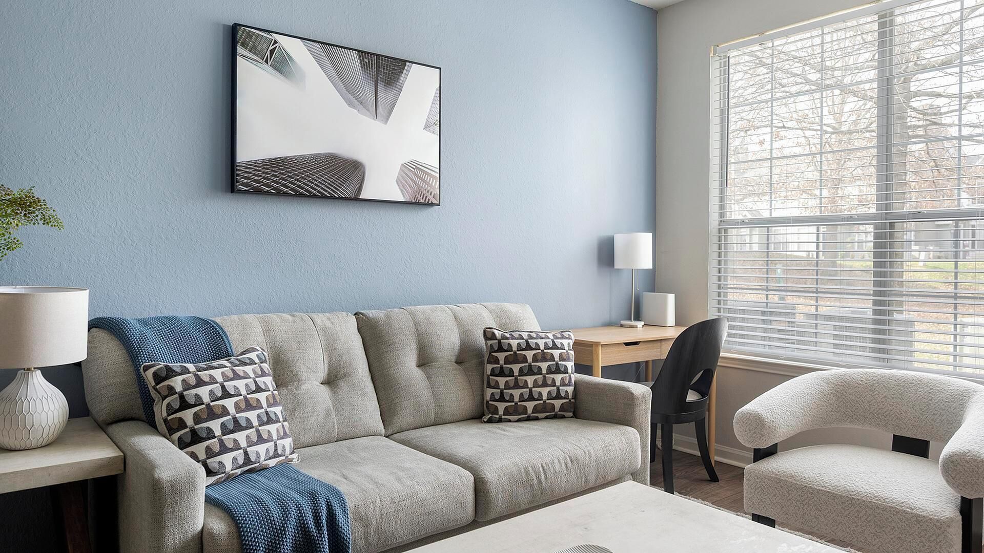 A living room with a sofa, two armchairs, a coffee table, a lamp, a side table, and a painting on the wall.