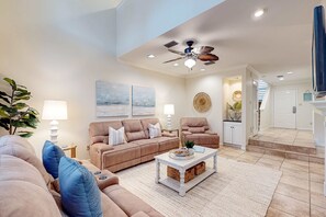 Ein Wohnzimmer mit einem beigefarbenen Sofa, einem weißen Couchtisch und einem Deckenventilator.