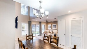 Ein Essbereich mit Holztisch und Stühlen, einer Chandelüster und Blick auf ein Wohnzimmer mit Sofa und Deckenventilator.