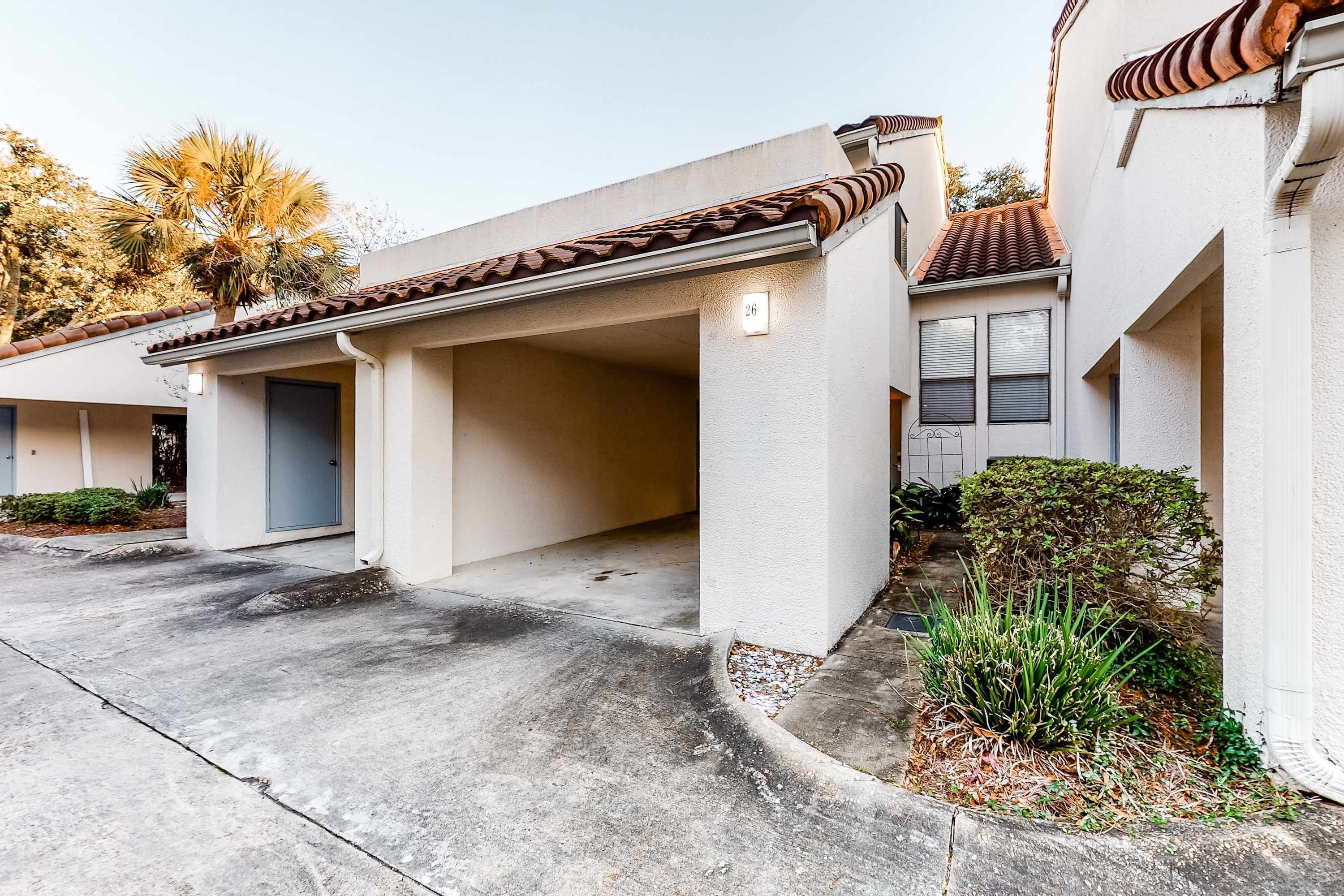 A residential building with a covered garage, a concrete driveway, and a small garden area with plants.