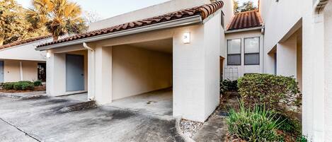 A residential building with a covered garage, a concrete driveway, and a small garden area with plants.