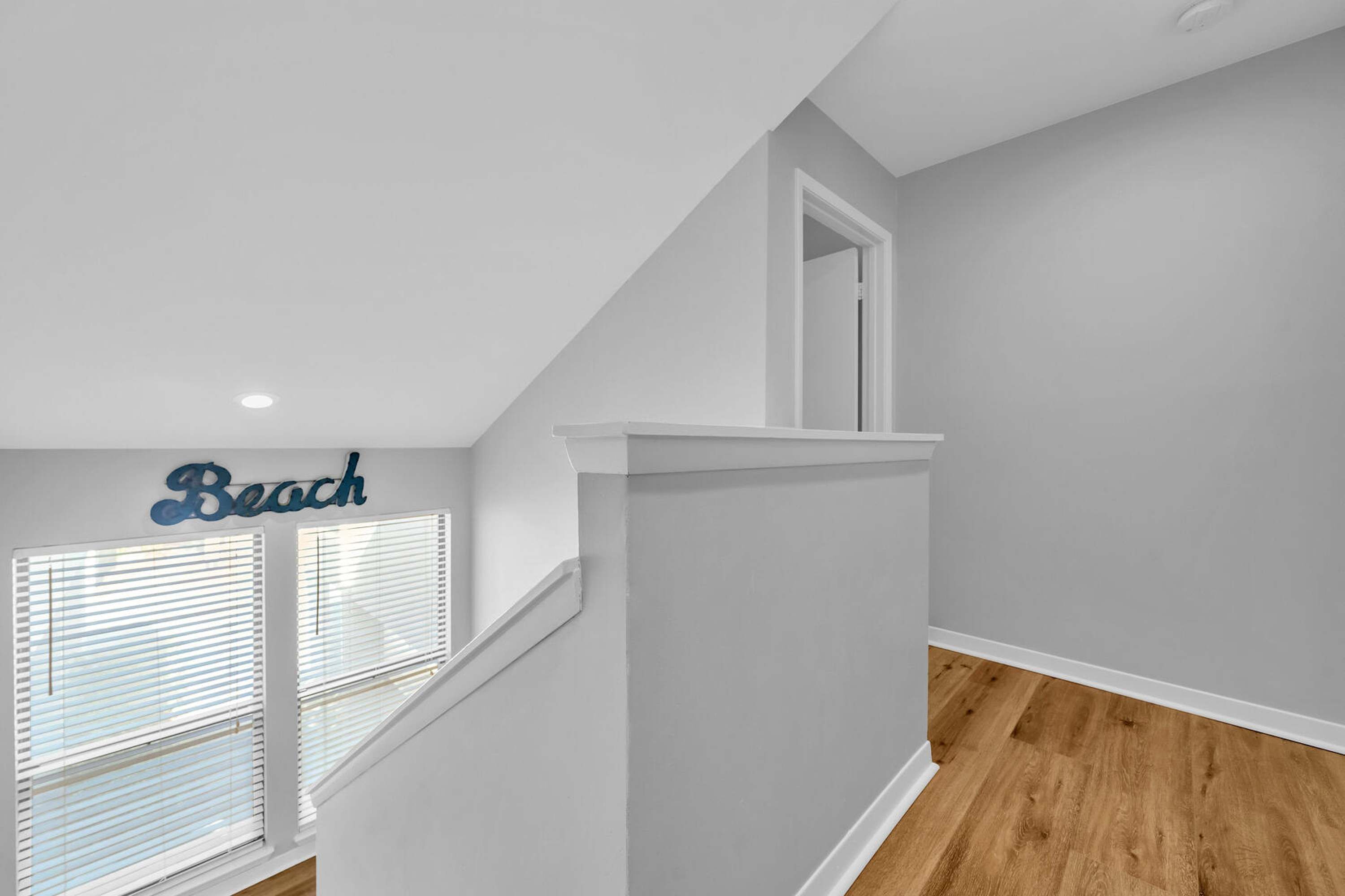 Un escalier avec une rampe blanche, une fenêtre avec des stores et un mur sur lequel est affiché un panneau indiquant « Plage ».