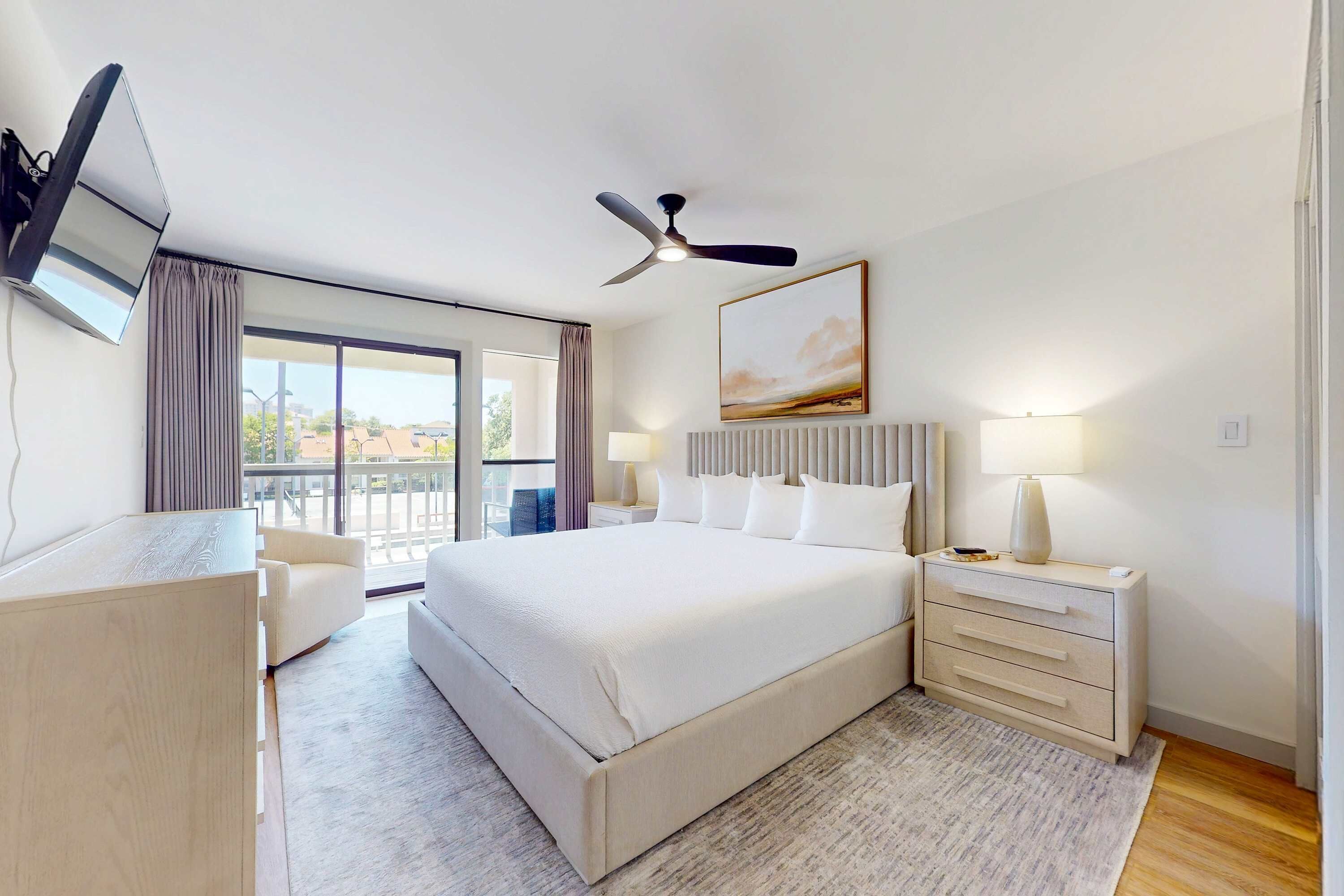Ein Hotelzimmer mit einem großen Bett, einem Schreibtisch, einem Stuhl, einem Deckenventilator, einem Gemälde und Blick ins Freie.