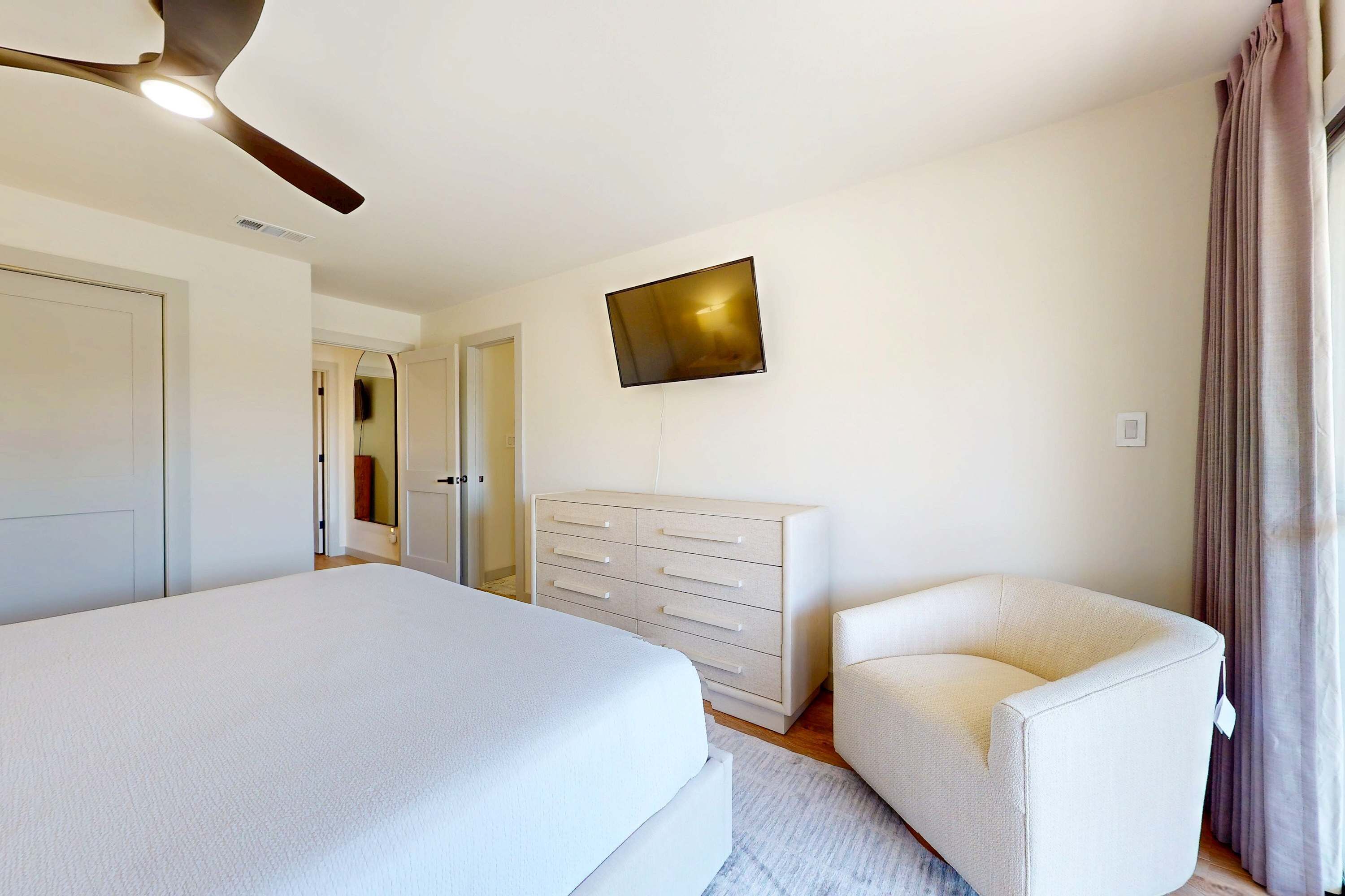 Une chambre à coucher comprenant un lit, une commode, une chaise, un téléviseur et un ventilateur de plafond.