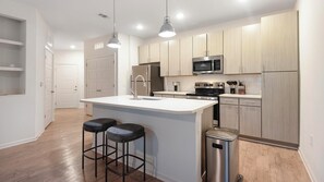 A modern kitchen with a central island, stainless steel appliances, and a bar stool seating area. - Landing | Modern 1BD, Gym, Pool (Memphis)