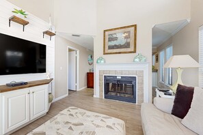 A living room with a fireplace, a television, and a sofa. - Exclusive 2BR Retreat: Steps to Beach & Tennis (Miramar Beach)