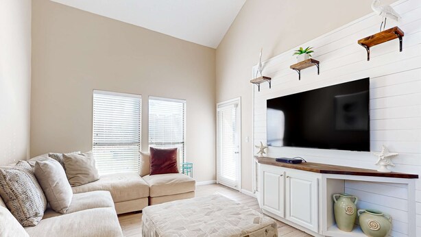Una sala de estar con sofá, reposapiés, televisor y objetos decorativos en estanterías.