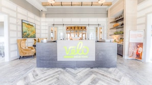 Un área de recepción con un mostrador central que muestra el logotipo 'velo shelby farms', un diseño moderno con suelo de espiga y un cuadro grande en la pared de la izquierda.