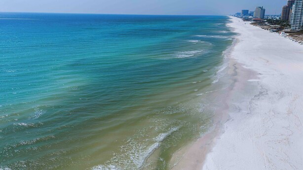 Ein Strand mit klarem Wasser, einem sandigen Ufer und hohen Gebäuden im Hintergrund.